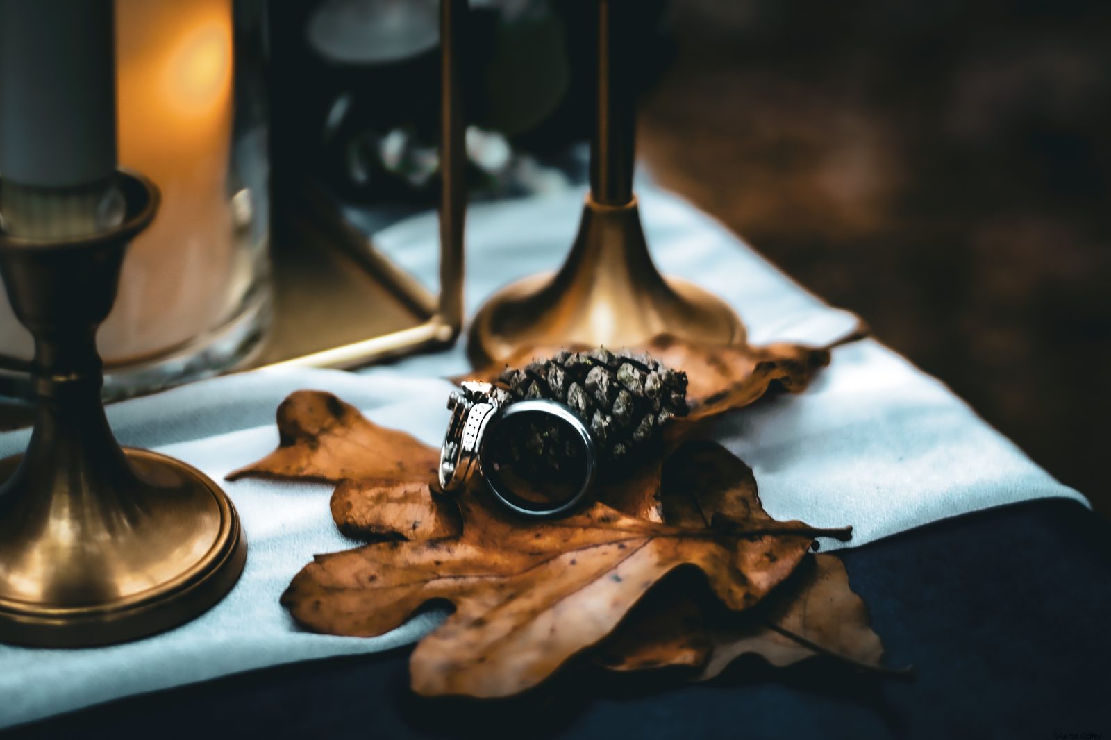 A wedding ring and band resting on an autumn oak leaf beside candlelight — a detail from an Oklahoma wedding.